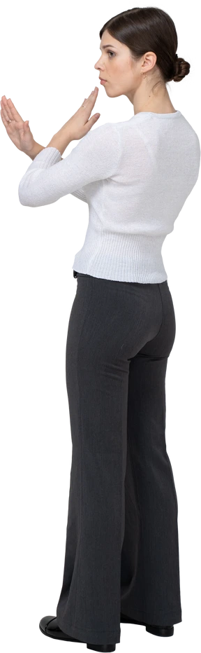 Three-quarter back view of a young woman in office clothing crossing arms