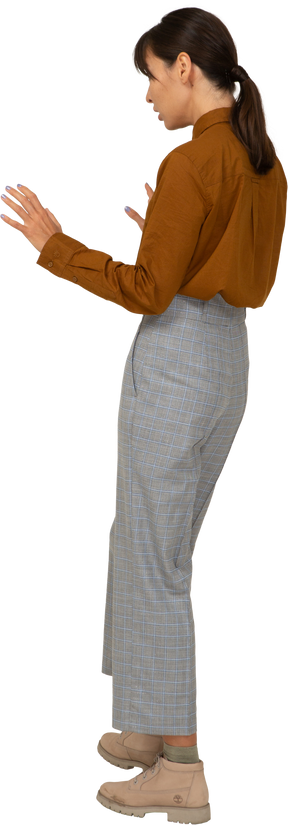 Vista posteriore di tre quarti di una giovane donna asiatica attenta in calzoni e camicetta che allunga le braccia