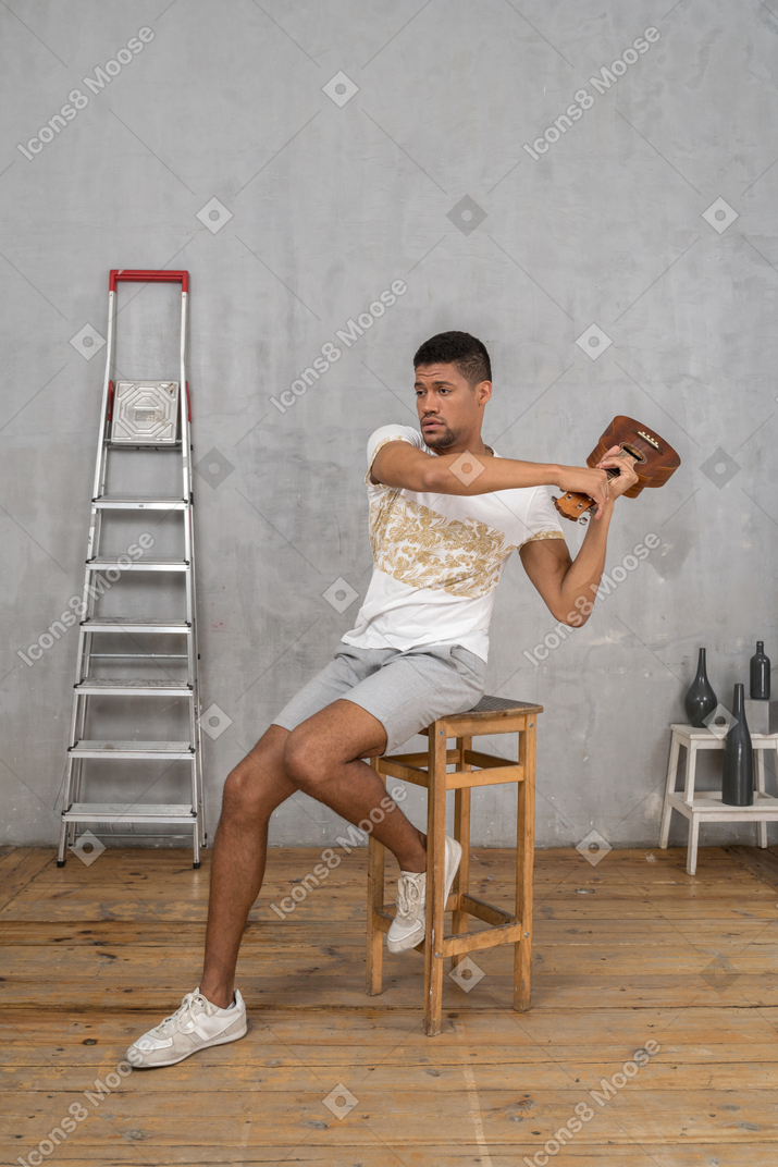 Vista de tres cuartos de un hombre en un taburete balanceando un ukelele