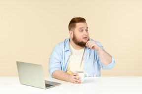 Interessiert an etwas jungem übergewicht, das vor einem laptop sitzt und tee trinkt