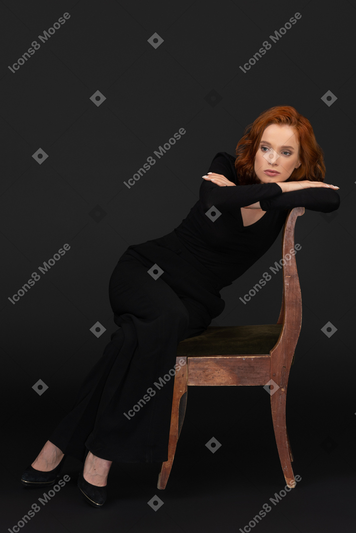 Cute young woman sitting on the wooden chair and looking to the left