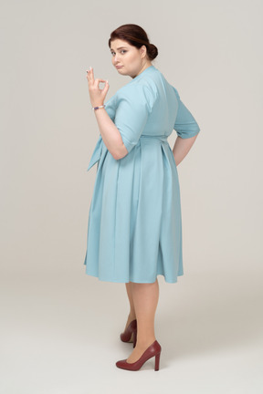 Vista lateral de uma mulher de vestido azul mostrando sinal de ok