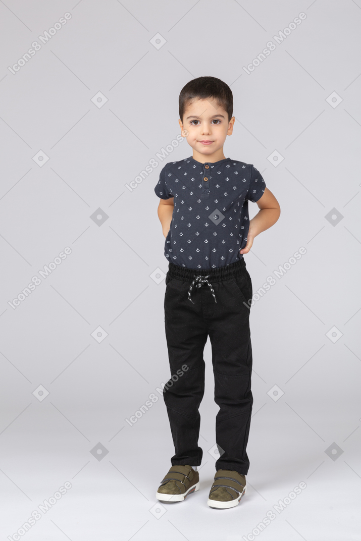Front view of a cute kid boy posing with hands on back and looking at camera