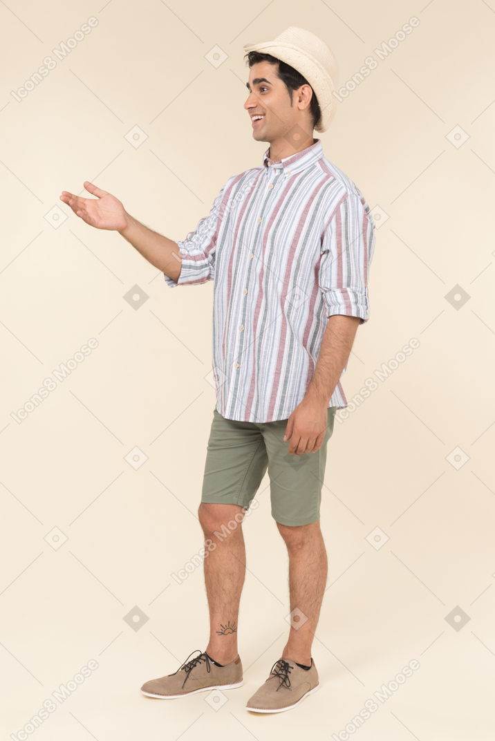 Smiling young guy seems like goes to beach and pointing forward with a hand