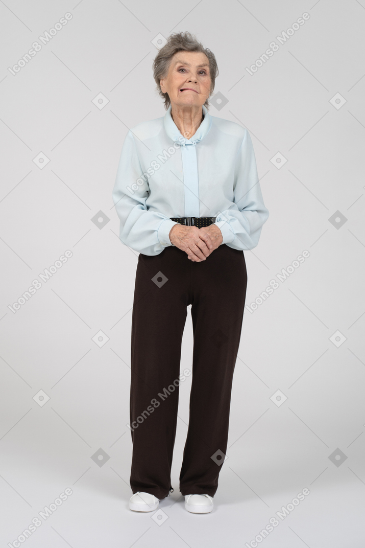 Vue de face d'une vieille femme grimaçant légèrement avec les mains jointes