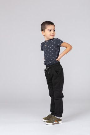 Vista lateral de um lindo menino em roupas casuais, posando com as mãos nas costas