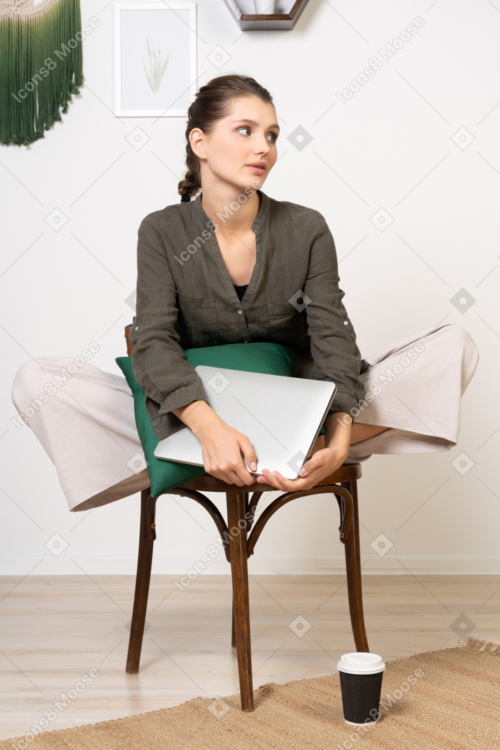 一个无聊的年轻女子坐在椅子上，拿着她的笔记本电脑的前视图
