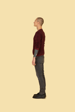 じっと立っている赤いセーターを着た若い男の側面図
