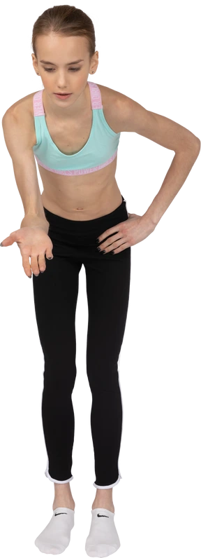 Front view of a teen girl in sportswear pointing hands somewhere down