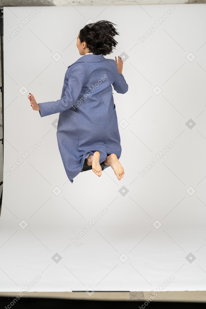 Vista trasera de una mujer con abrigo saltando con las piernas dobladas