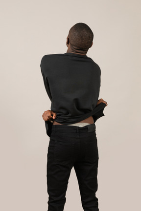 Back view of young man taking off his sweatshirt