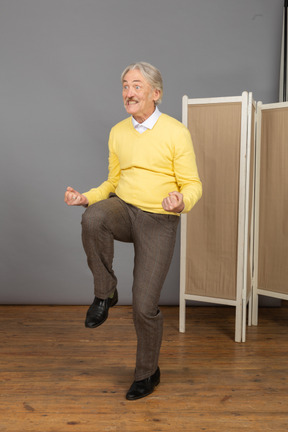 Three-quarter view of a happy old man clenching fists and raising his leg