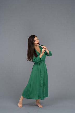 Three-quarter view of a young lady in green dress playing flute while leaning back