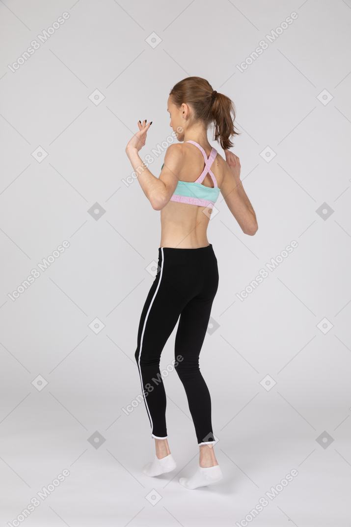 Vista posterior de tres cuartos de una jovencita en ropa deportiva caminando cautelosamente de puntillas