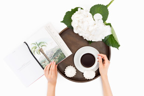 Tazza di caffè, meringhe, fiore bianco e libro sul vassoio rotondo in legno