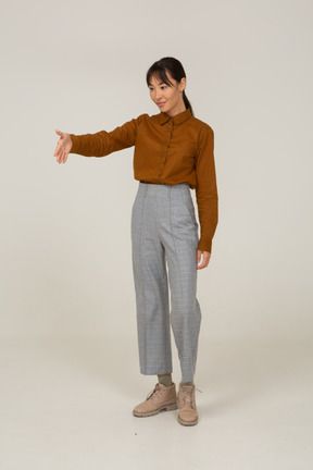 Vista di tre quarti di una giovane donna asiatica che saluta in calzoni e camicetta che tende la mano