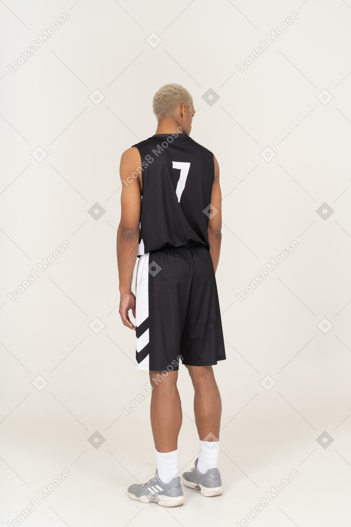 Vue de trois quarts d'un jeune joueur de basket-ball masculin immobile et regardant de côté