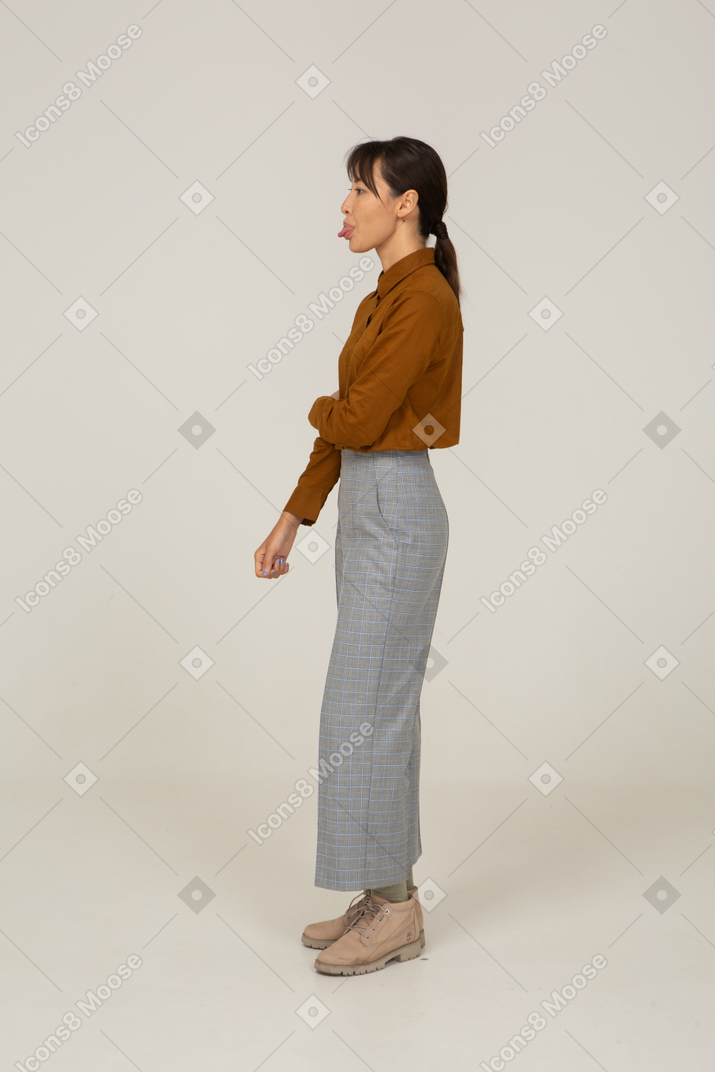 一位身着马裤和衬衫的年轻亚洲女性的侧视图，触摸手臂并展示舌头