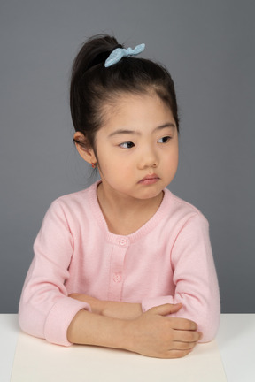 Серьезная маленькая девочка сидит за столом