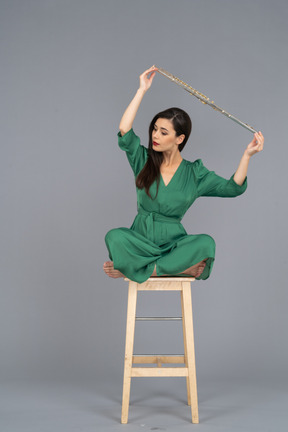 Full-length of a young lady holding her clarinet over head while sitting on a wooden chair