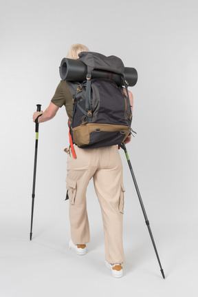 Female tourist carrying backpack and walking with sticks back to camera