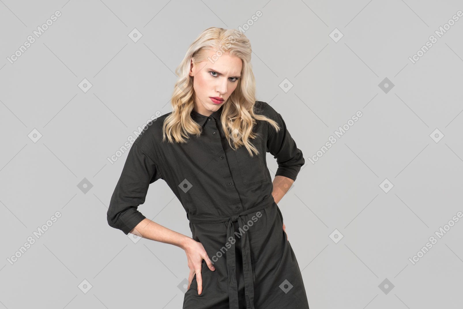 Una joven rubia en un vestido negro de pie contra el fondo gris liso