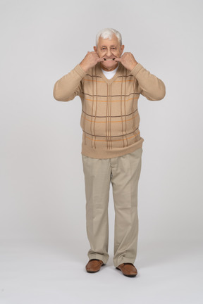 Front view of an old man in casual  clothes putting fingers in mouth
