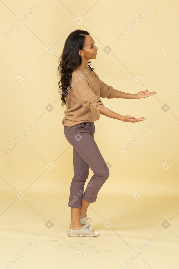 Vista lateral de una mujer joven de piel oscura extendiendo sus manos