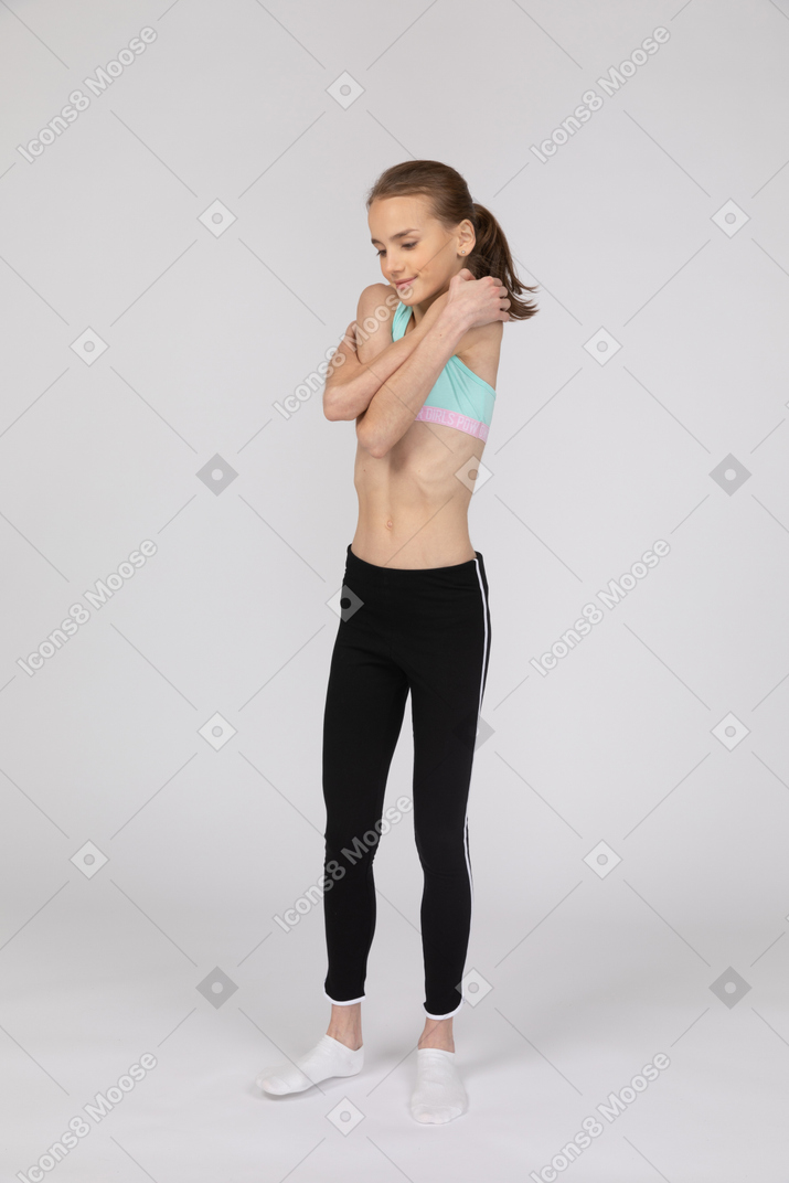 Vista de tres cuartos de una jovencita en ropa deportiva abrazando a sí misma