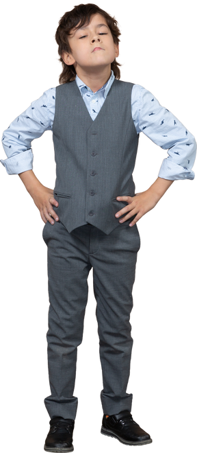 Vista frontal de un chico lindo con traje gris posando con las manos en las caderas y mirando hacia arriba