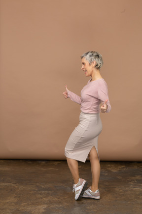Vista lateral de una mujer feliz en ropa casual mostrando los pulgares para arriba