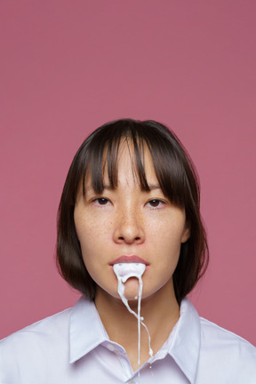 Close-up of a young female in shirt looking at camera and spilling milk out of mouth