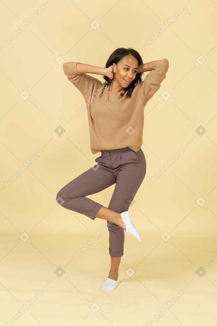 Vista frontal de una mujer joven de piel oscura levantando la pierna mientras toca la cabeza