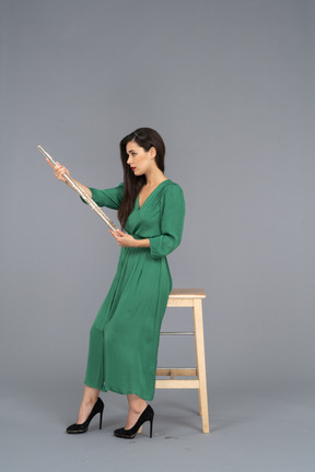 Vista laterale di una giovane donna in abito verde, seduta su una sedia e tenendo il clarinetto