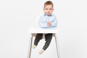 Очаровательный улыбающийся малыш сидит в детском стульчике