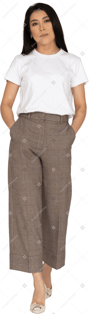 Vista frontale di una giovane donna annoiata a piedi in calzoni e t-shirt mettendo le mani in tasca