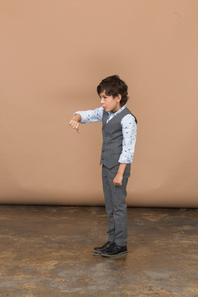 Vista lateral de um menino de terno cinza, mostrando o polegar para baixo