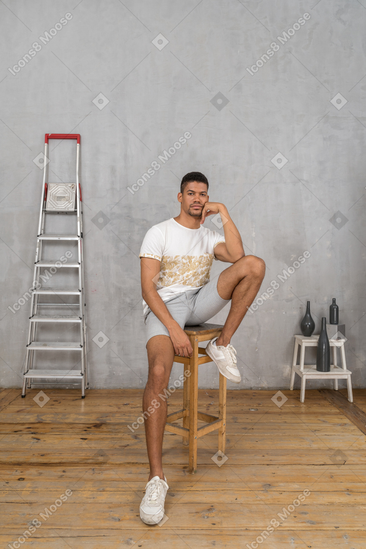 Entspannter junger mann, der auf hocker sitzt