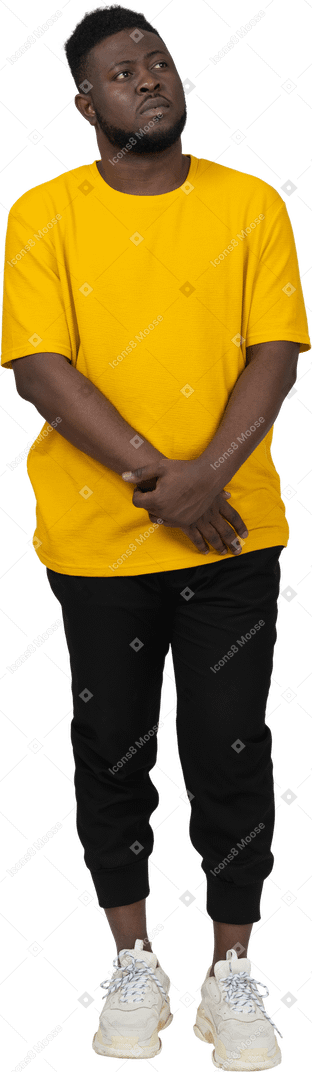 Front view of a shy young dark-skinned man in yellow t-shirt holding hands together