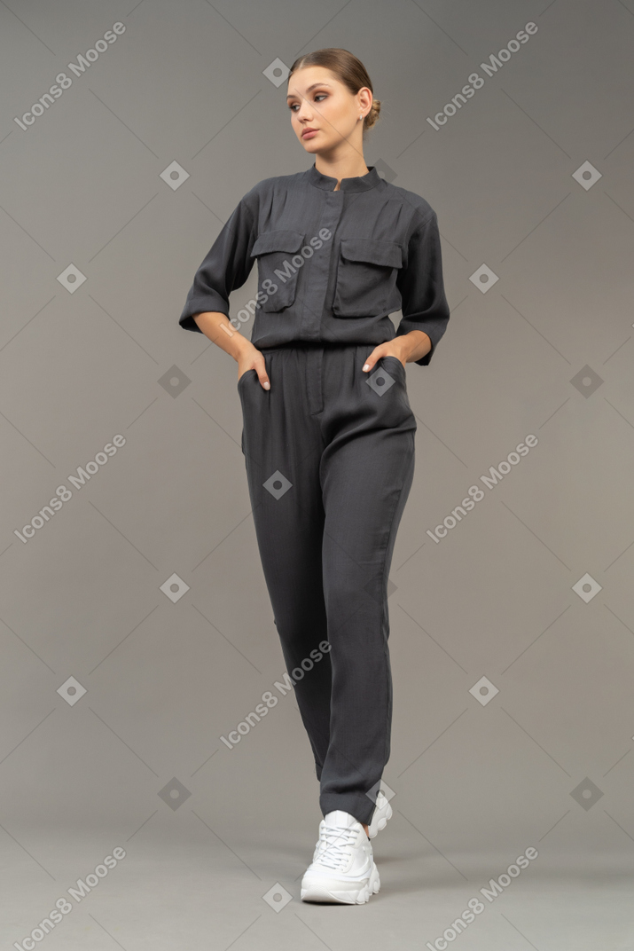 Front view of a walking young woman in a jumpsuit holding hands in pockets