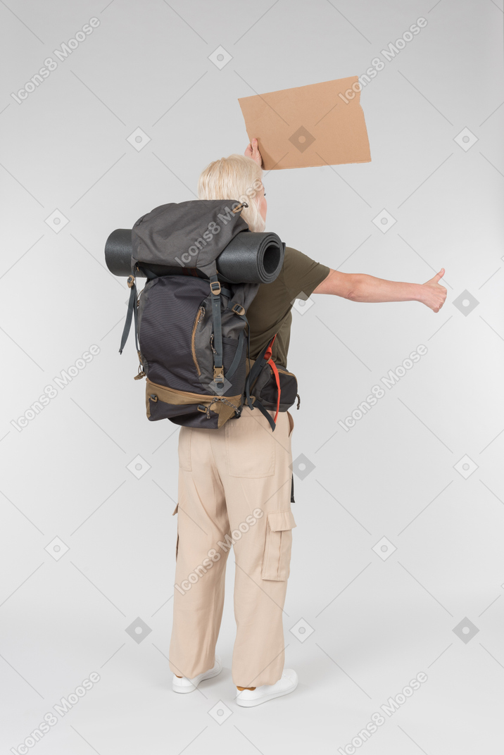 Female tourist hitchhiker carrying backpack and standing back to camera