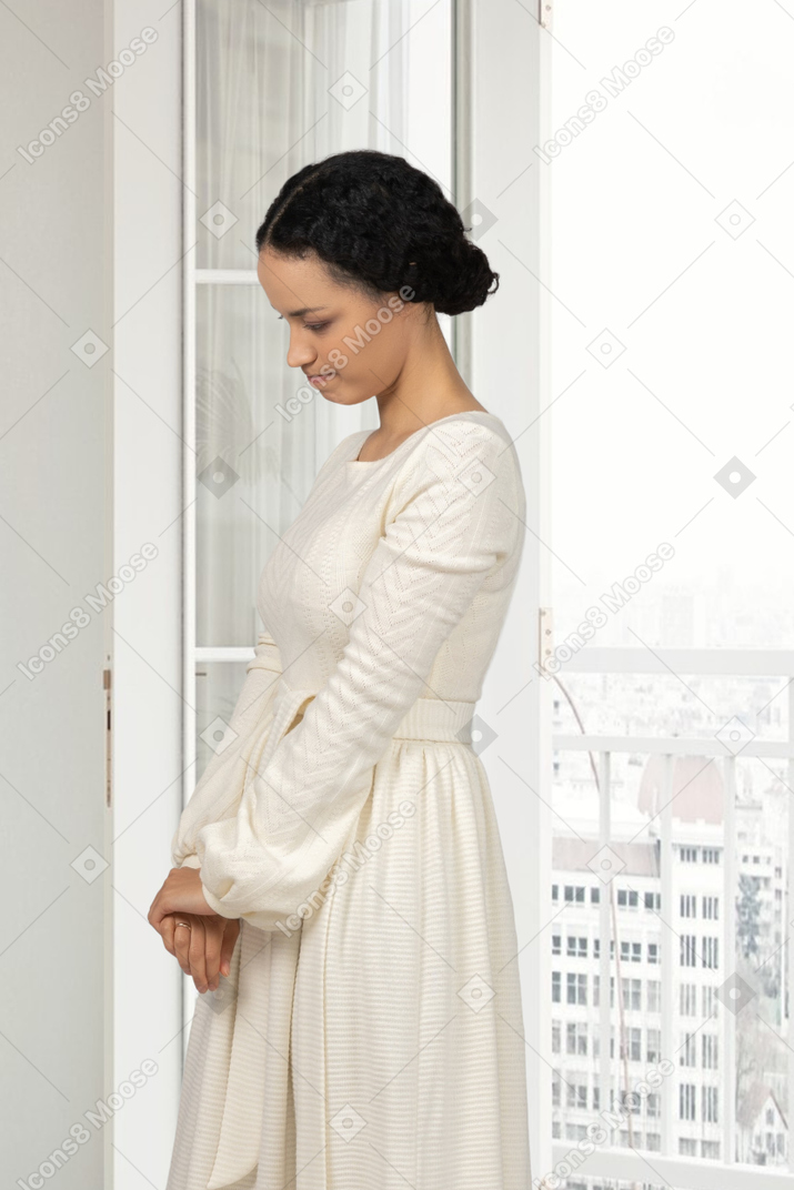 Uma mulher em um vestido branco em frente a uma janela