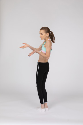Three-quarter back view of a perplexed teen girl in sportswear outstretching hands