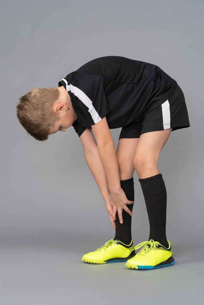 Three-quarter view of a child boy in football uniform leaning forward and touching tiptoes