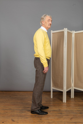 Side view of an old man standing still looking at camera