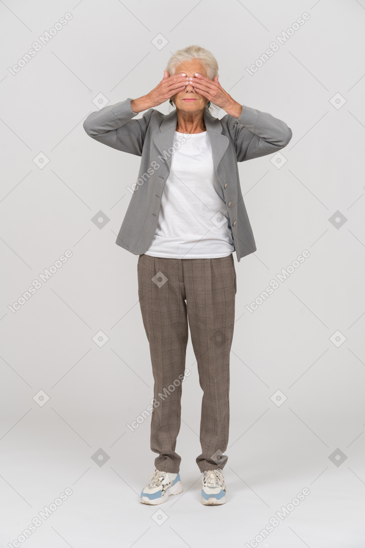 Front view of an old lady in suit covering eyes with hands