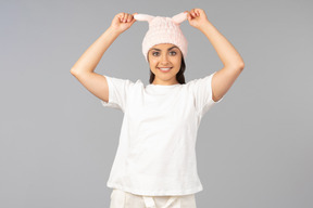 Young indian woman in home clothes touching pink rabbit like hat she's wearing