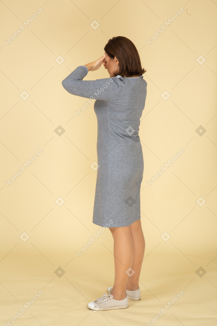 Vista laterale di una donna in abito grigio che chiude gli occhi con le mani