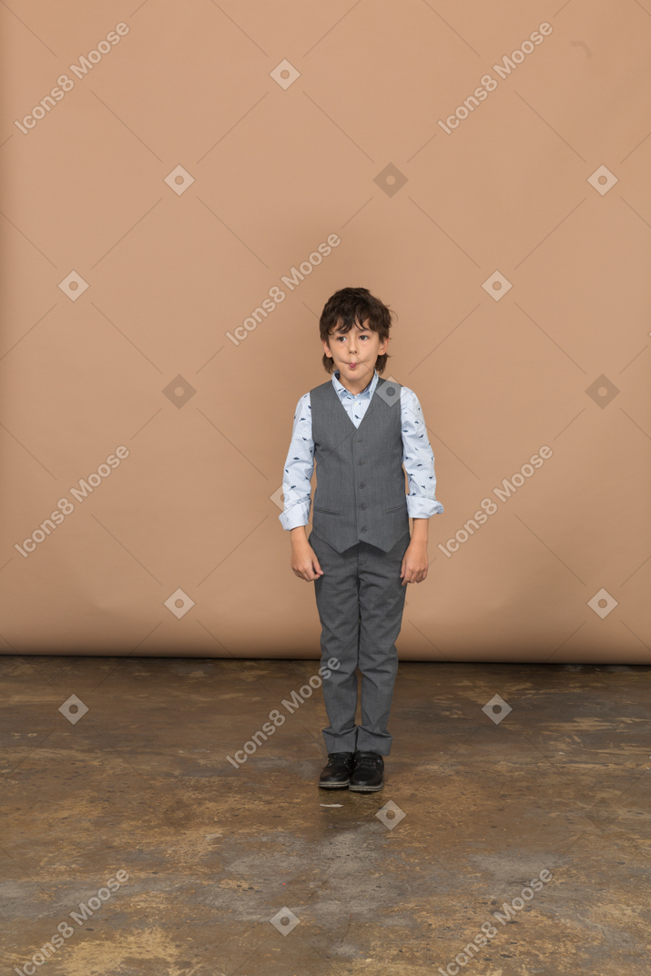 一个穿着西装的男孩站着不动做鬼脸的前视图
