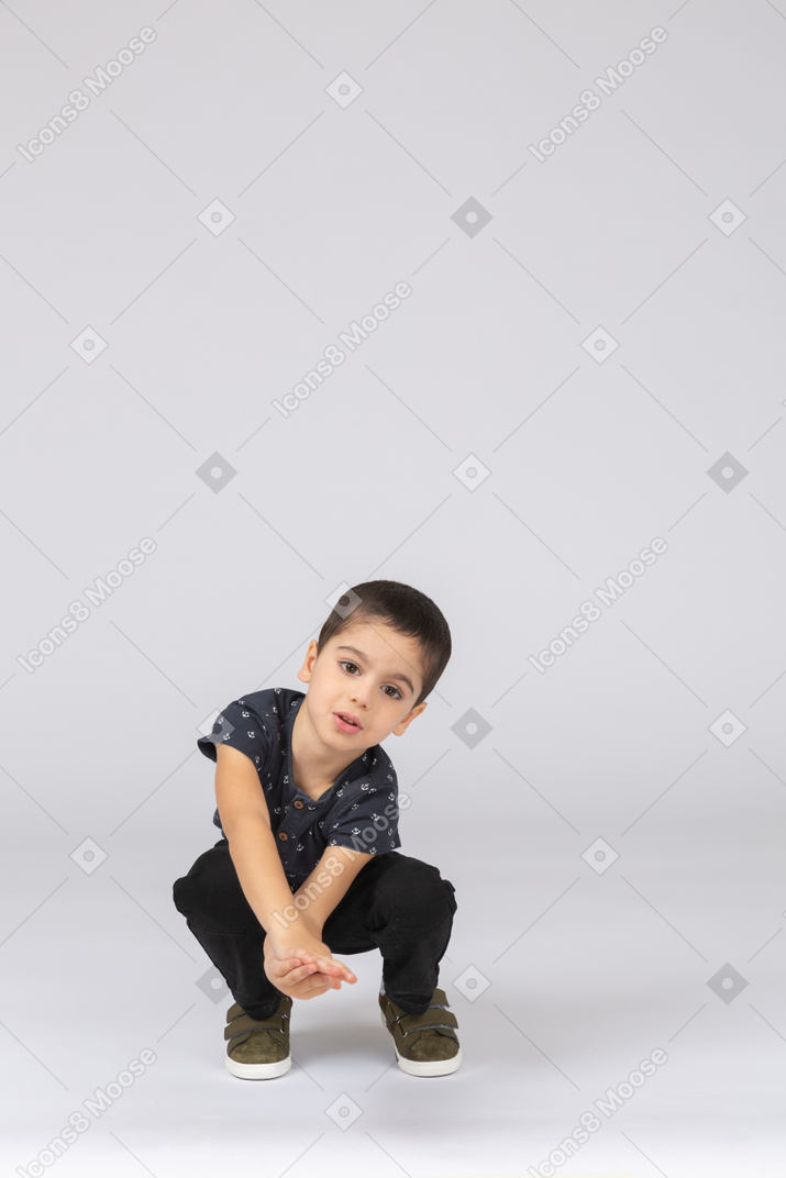 Vista frontal de un chico lindo en cuclillas y mirando a la cámara